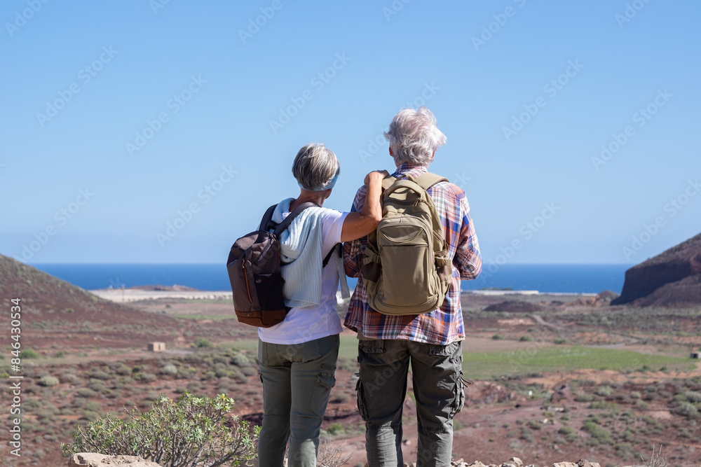 Rear view of Senior active couple in outdoor activity in mountain admiring the landscape enjoying healthy lifestyle and freedom in summer vacation. Blue sky and horizon over the water