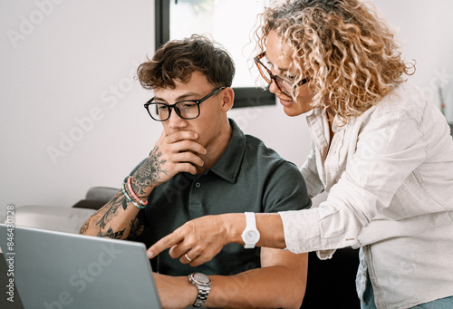 Young smiling boy studies at home with the support of a personal tutor using laptop. Blonde teacher follows the instruction of a handsome boy. Concept of modern education with the use of technology