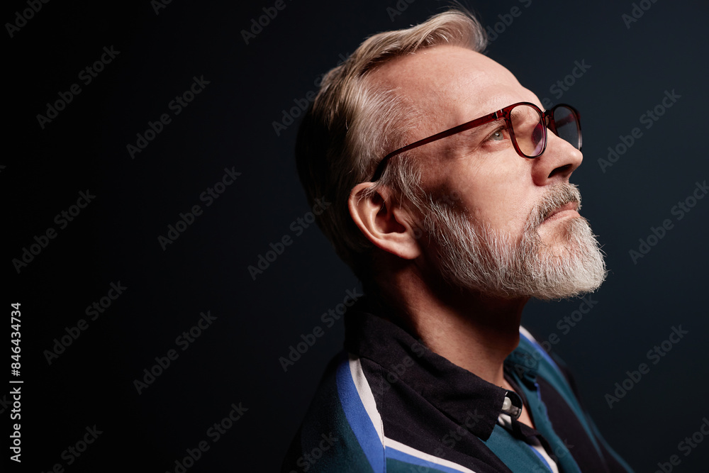 Side view portrait of bearded senior man wearing glasses on dark background, copy space Side view portrait of bearded senior man wearing glasses on dark background, copy space