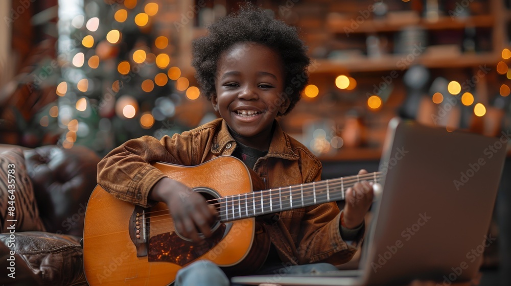 A cheerful Afro-American boy, 9 years old, is learning to play the guitar online while sitting at a laptop monitor while at home. learning to play guitar remotely A cheerful Afro-American boy, 9 years old, is learning to play the guitar online while sitting at a laptop monitor while at home. learning to play guitar remotely