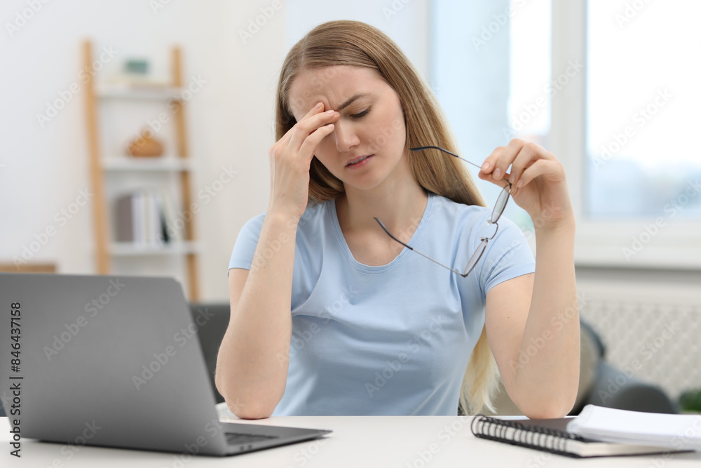 Overwhelmed young woman sitting with laptop at table in room Overwhelmed young woman sitting with laptop at table in room