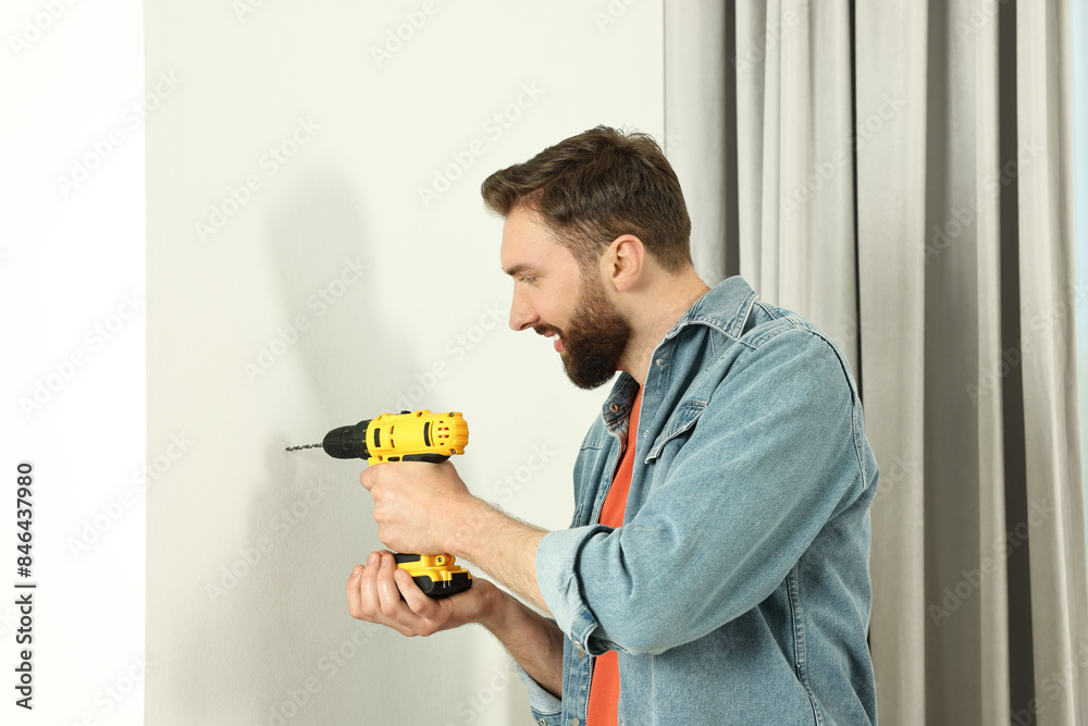 Smiling man drilling white wall at home