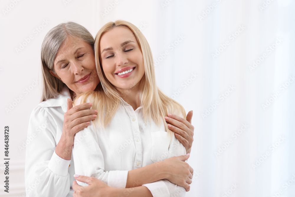 Family portrait of young woman and her mother near white wall. Space for text Family portrait of young woman and her mother near white wall. Space for text