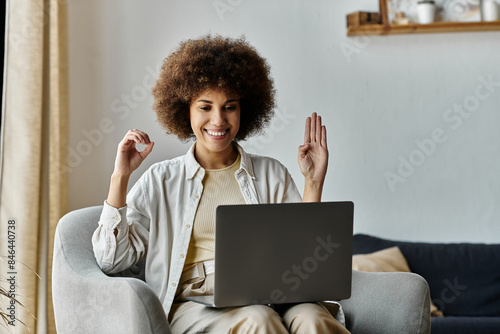 A woman sitting on a couch, using sign language while on a video call on her laptop.