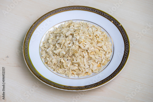 Flattened rice on a white plate on wooden background. It is also known as chiwda, chira, pohe, aval, pauwa, sira, chivda, or avalakki. photo