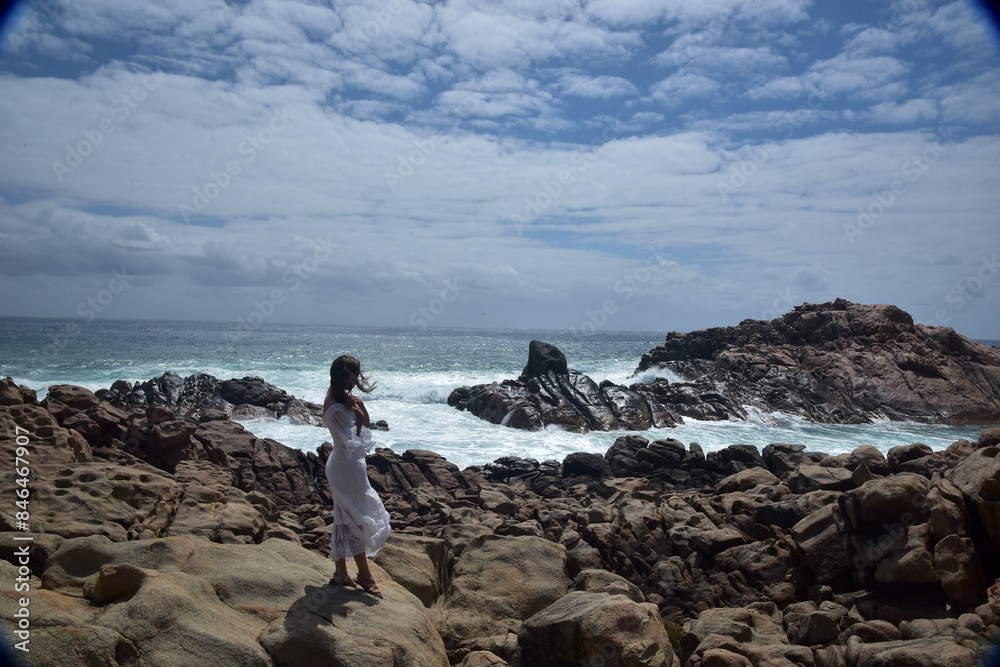 portrait of female model standing wearing white goddess dress, dramatic natural landscape background of rocky ocean shoreline with stone clifftops. castle rock, Busselton, Western Australia portrait of female model standing wearing white goddess dress, dramatic natural landscape background of rocky ocean shoreline with stone clifftops. castle rock, Busselton, Western Australia