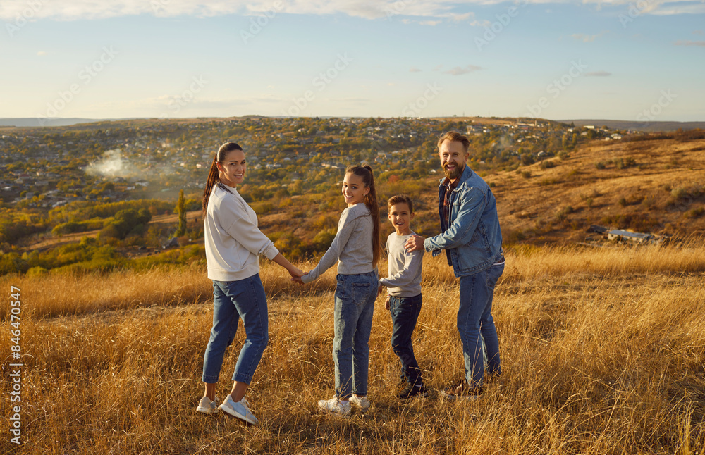 Happy family of four holding hands enjoying beautiful nature standing in the field together. Young smiling parents with two children walking outdoors. Concept of happy family and relationships. Happy family of four holding hands enjoying beautiful nature standing in the field together. Young smiling parents with two children walking outdoors. Concept of happy family and relationships.