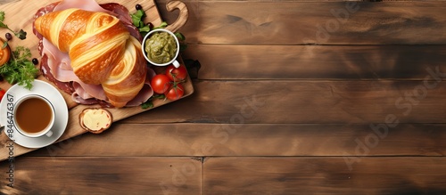 Top view image of a croissant sandwich with ham cheese and vegetables served on a wooden cutting board accompanied by a cup of coffee Plenty of room for additional content in the picture photo