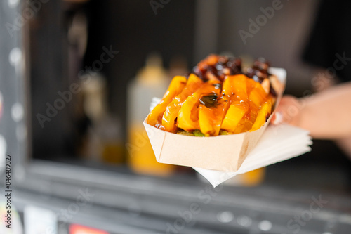 Close-up view of a hand holding a paper container filled with fries and toppings, perfect for food-related themes.