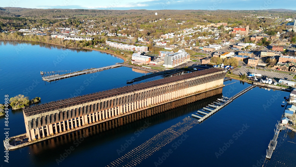 An aerial view of a large dock with arch structures with a cityscape and forests backdrop