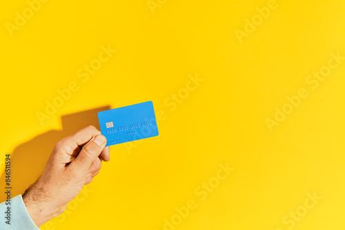 Male hand holds blue plastic bank card over yellow background with copy space