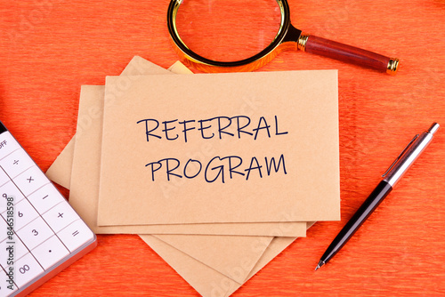 Business concept. Words REFERRAL PROGRAM on postal envelopes in a composition with a calculator, magnifying glass and pen on an orange background