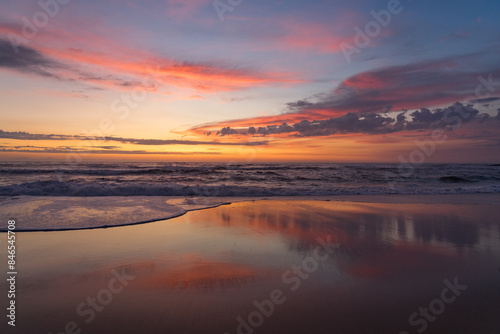 Sunset landscape of a beautiful and paradisaical beach with the clouds reflected on the water. Summer and vacations concept background.
