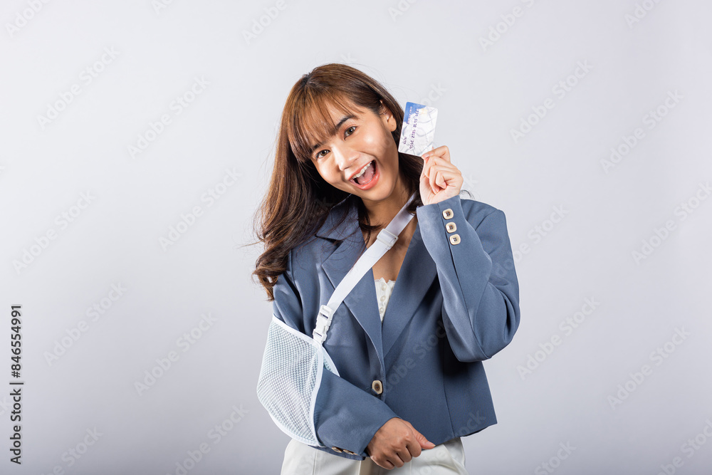 Injured woman, smiling despite her broken arm, dons a treatment splint. Emergency medical bills paid with a credit card. Happy Asian female with sling support isolated on white. Injury is visible. Injured woman, smiling despite her broken arm, dons a treatment splint. Emergency medical bills paid with a credit card. Happy Asian female with sling support isolated on white. Injury is visible.