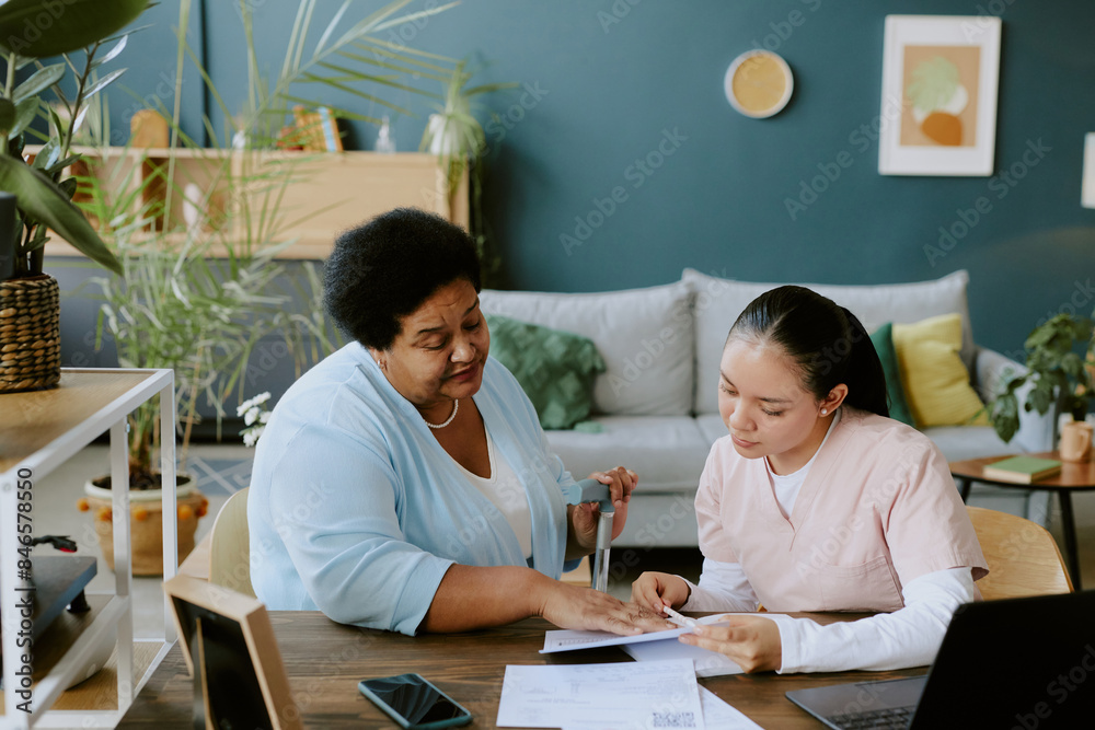 Nurse in rose scrubs familiarizing African American female patient with form in calm atmosphere Nurse in rose scrubs familiarizing African American female patient with form in calm atmosphere