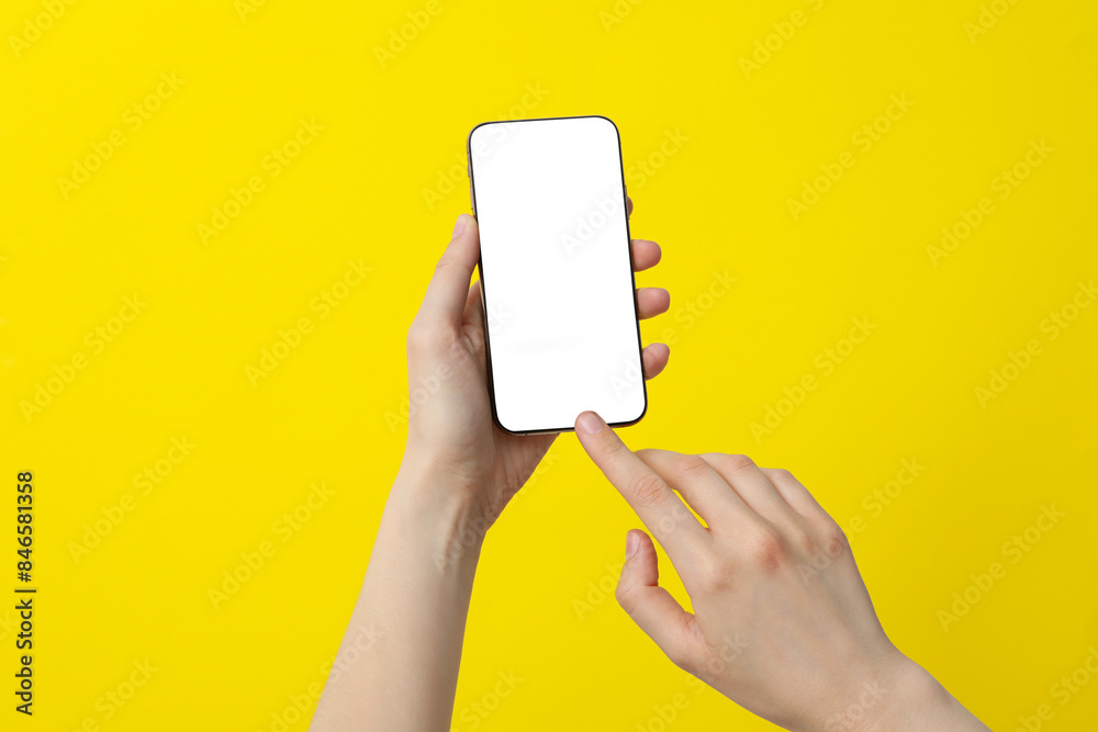 Female hand holding a smartphone on a yellow background Female hand holding a smartphone on a yellow background