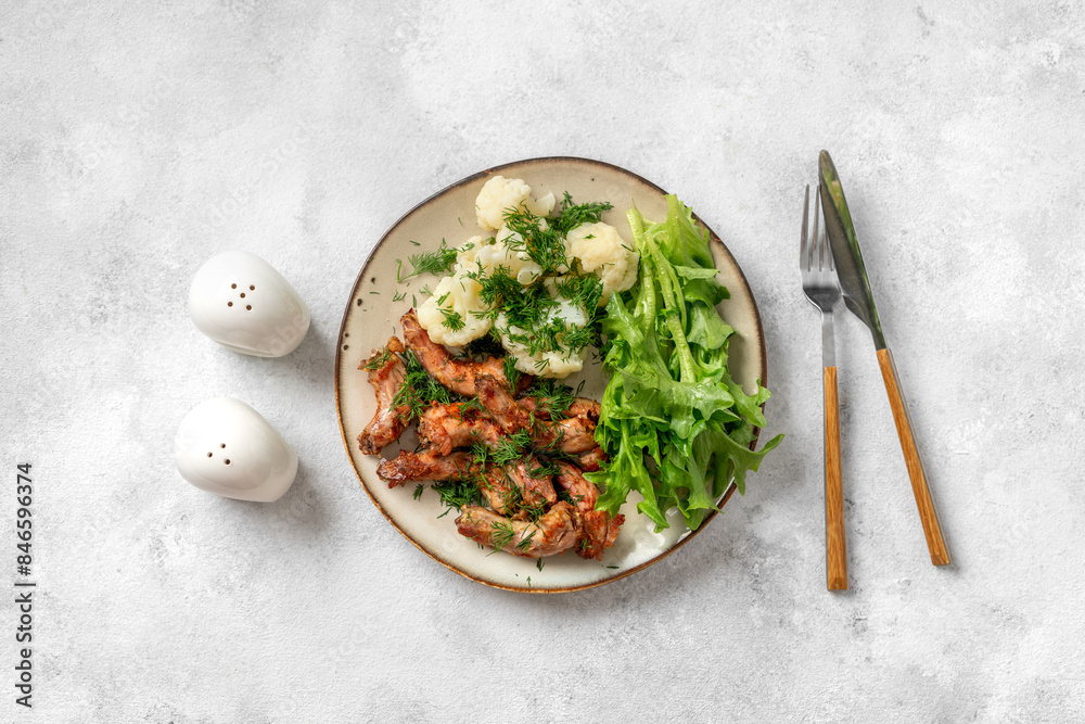 Baked or fried chicken necks in barbecue sauce, cauliflower and lettuce leaves on a plate on the table. A healthy dinner on a light gray background. Proper nutrition. Top view
