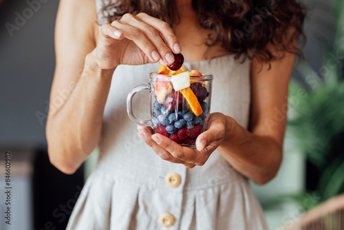 Wallpaper Mural Close-up of a glass mug with fruits and berries in a female well-groomed hands. A young woman in a sundress is eating cherries at home. Torontodigital.ca