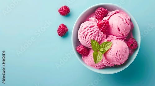 Bowl of raspberry ice cream scoops with fresh berries on pastel blue background, top view.