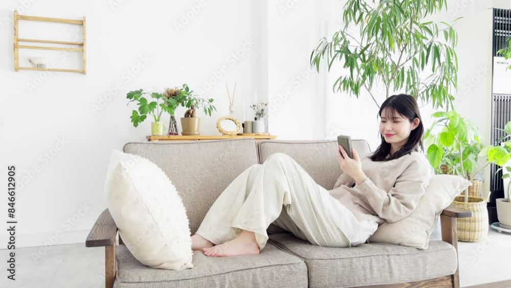 ソファでくつろぎながらスマホを見る女性 ソファでくつろぎながらスマホを見る女性