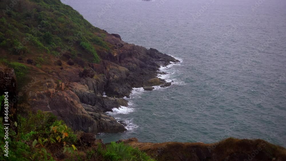 A picturesque view of rugged coastal cliffs with lush greenery overlooking the calm, blue ocean waters at Kudle Beach, Gokarna.