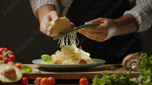 Chef grates hard cheese on top of a freshly prepared pasta dish, Pasta is mediterranean Italian traditional cuisine.
