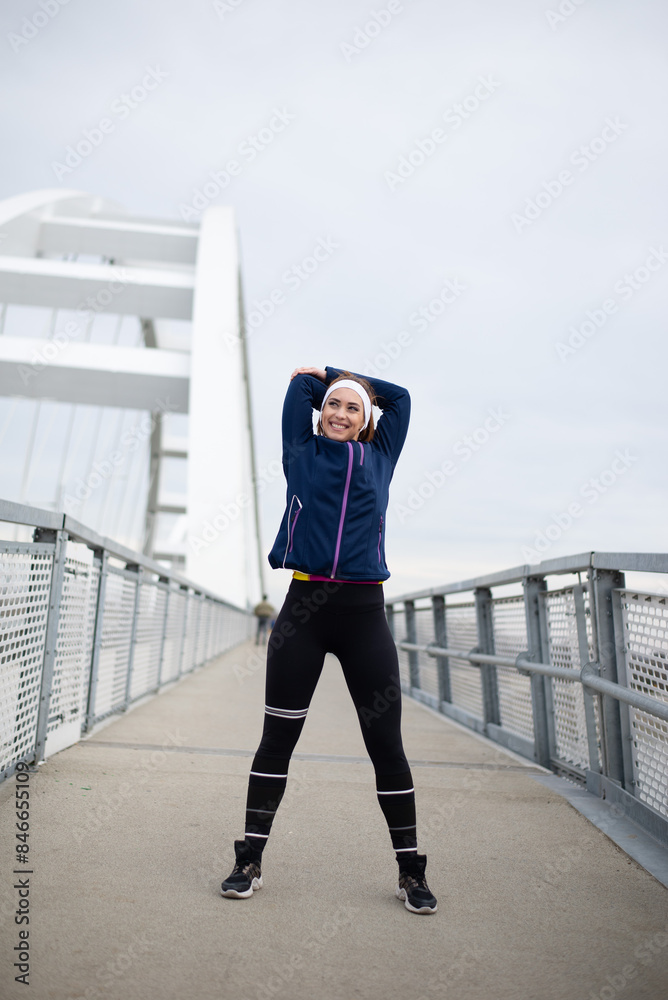 Fototapeta premium Young smiling woman exercising on the bridge, stretching and warming up