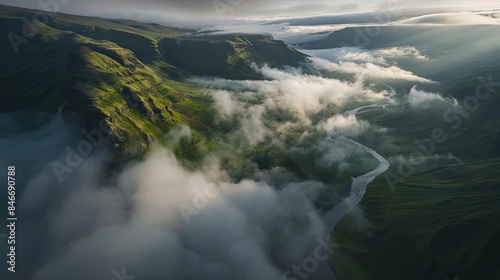 Aerial view of a misty river winding through green, mountainous landscape under dramatic clouds, capturing the beauty of nature and tranquility.