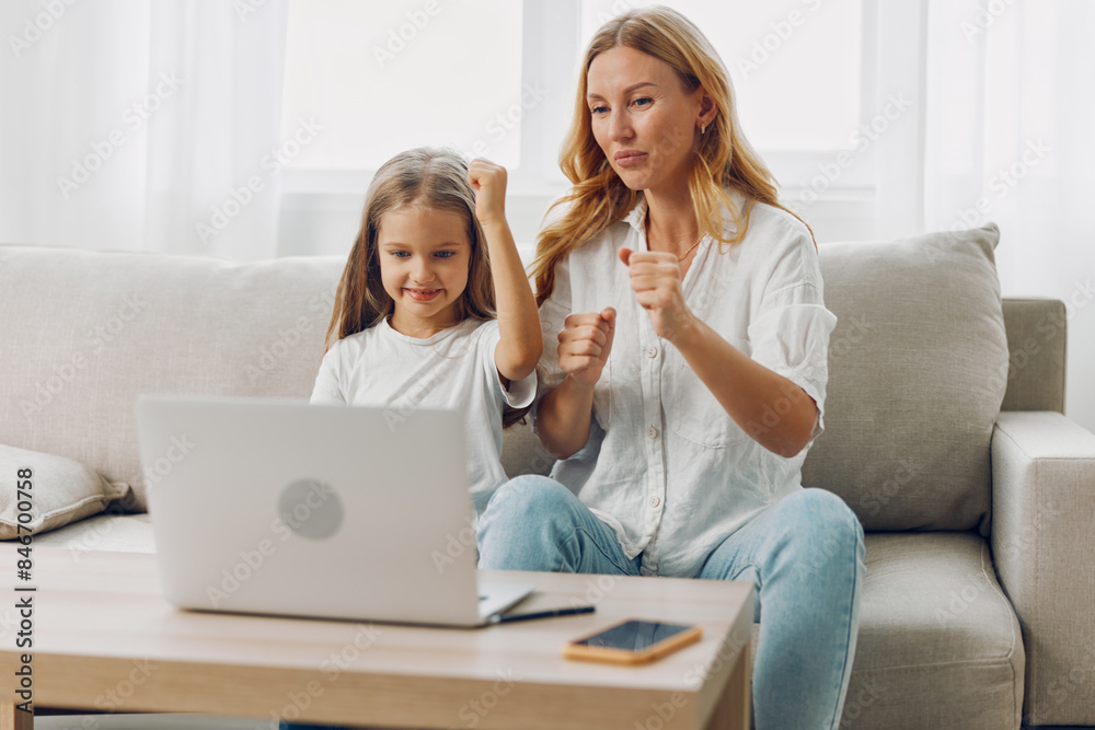 Excited woman and young girl sitting on a cozy couch raising hands in celebration while using a laptop Excited woman and young girl sitting on a cozy couch raising hands in celebration while using a laptop