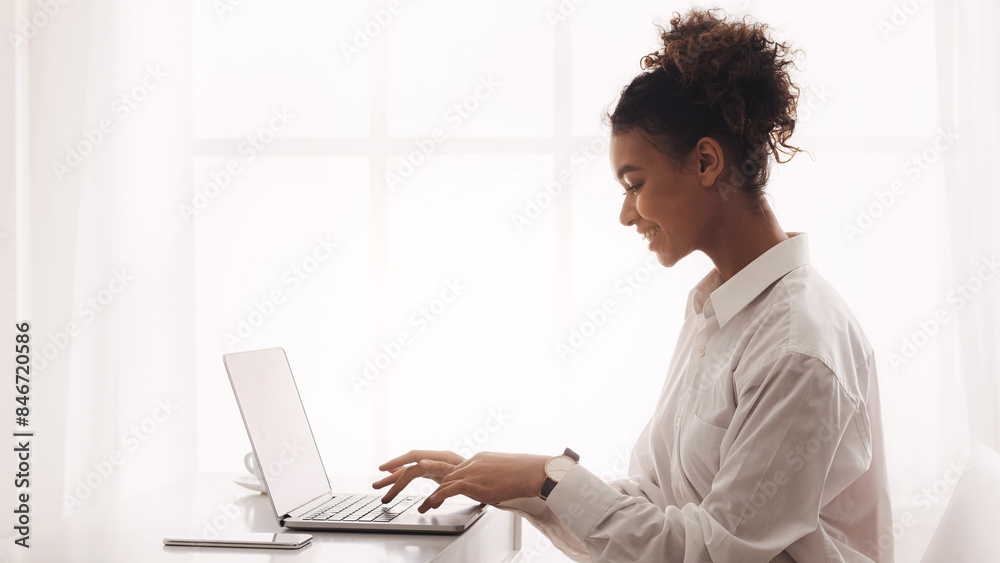 Freelancer woman working on laptop, typing on keyboard against window Freelancer woman working on laptop, typing on keyboard against window