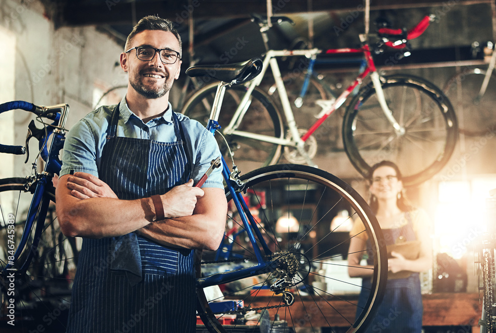 Obraz premium Man, portrait and arms crossed at work in bicycle repair shop or maintenance garage. Bike, mechanic and service with a professional handyman for startup, small business and workshop for fixing