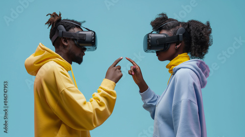 Homem e mulher africanos em moletons apontam um para o outro enquanto usam fones de ouvido VR em um fundo azul, foto de estoque para uma campanha publicitária