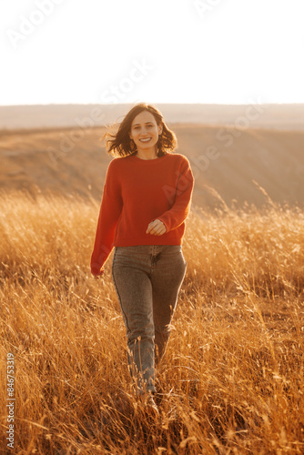 A woman in a red sweater walks through a sunny golden field, embodying autumn vibes with a relaxed and joyful attitude