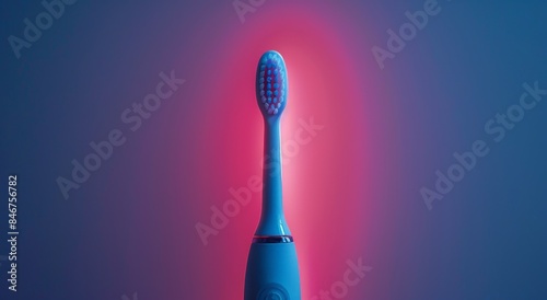 A white electric toothbrush with blue bristles and a black handle standing upright in front of a pink background.