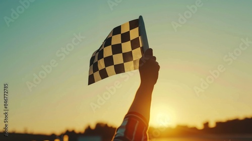 Hand holding a checkered race flag, waving it in the air against a clear sky