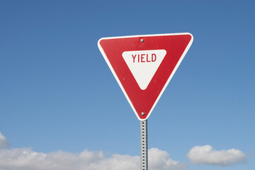 YIELD sign isolated against a blue sky background. A yield or give way sign indicates that merging drivers must prepare to stop if necessary to let a driver on another approach proceed.