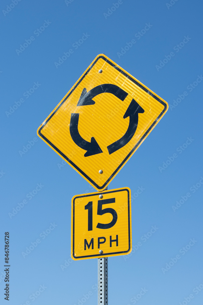Roundabout and speed limit signage isolated against a clear blue sky background. Roundabout and speed limit signage isolated against a clear blue sky background.