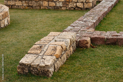 A detailed view of ancient stone ruins set on a green field, revealing historic masonry craftsmanship photo