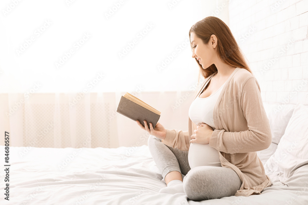 Time for hobby and relax. Smiling pregnant woman reading her favorite book, sitting on bed, free space Time for hobby and relax. Smiling pregnant woman reading her favorite book, sitting on bed, free space