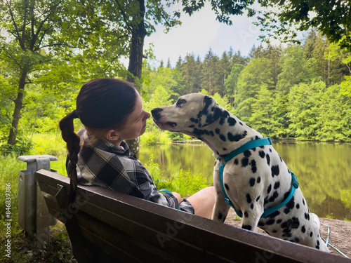 Girl and a dog sitting on a bench against the background of a lake in the forest photo