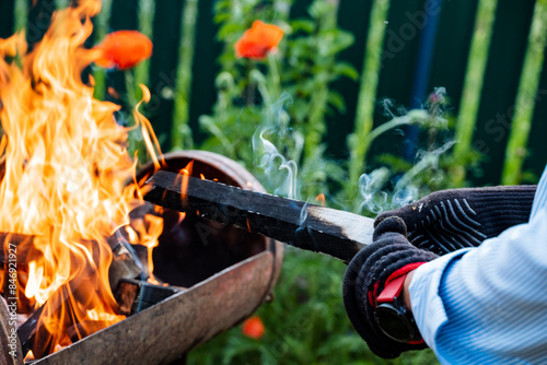 In an outdoor setting, a skilled blacksmith is seen shaping and molding metal using gloves and tongs over open fire, displaying traditional craftsmanship techniques photo