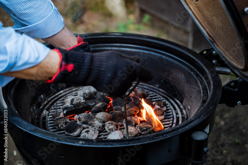 Obraz na płótnie A man is safely lighting charcoal on a grill for an outdoor BBQ preparation, wearing safety gloves