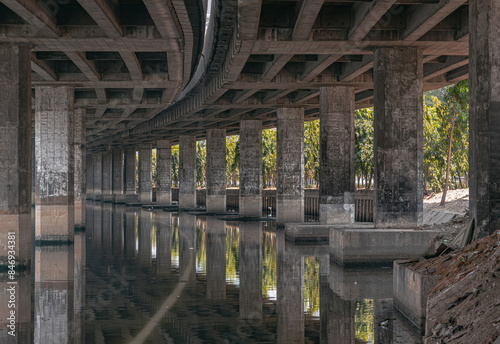 Perspective view of concrete pillars under Khlong Toei Expressway, with calm surface water reflection wonderful shadow, shape, lines and curve the underside support beams of the road along the Khlong. photo