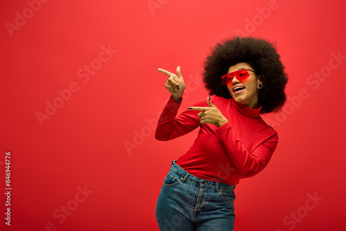 Stylish African American woman striking a pose in trendy red shirt and sunglasses.