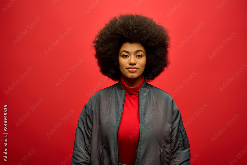 Stylish African American woman with curly hairdostands confidently against bright red backdrop. Stylish African American woman with curly hairdostands confidently against bright red backdrop.