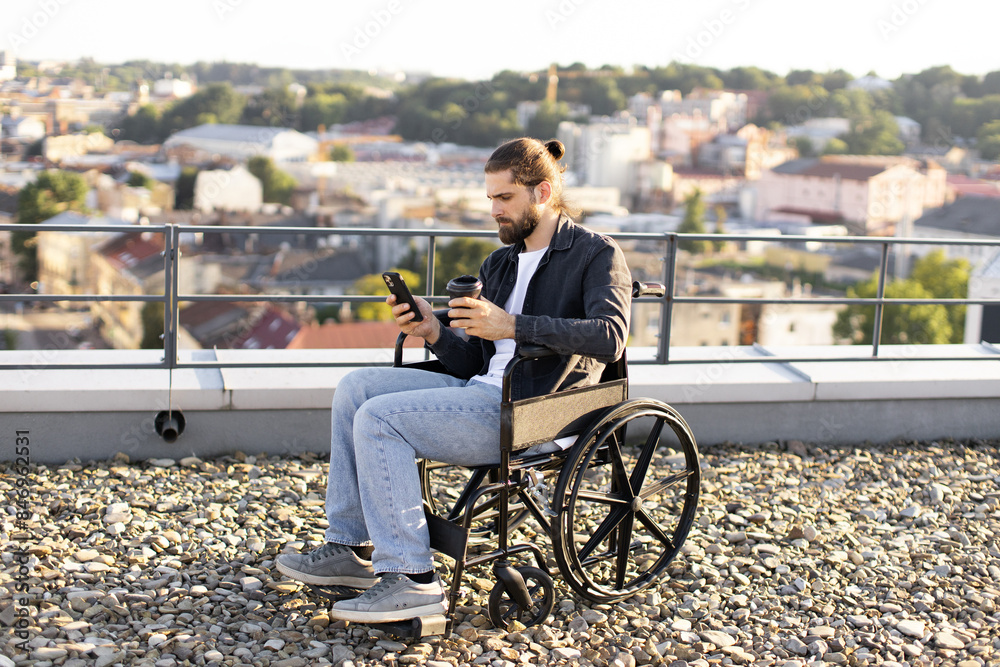 Young man in wheelchair using smartphone on rooftop overlooking cityscape. Concept of accessibility, modern technology, and urban lifestyle. Young man in wheelchair using smartphone on rooftop overlooking cityscape. Concept of accessibility, modern technology, and urban lifestyle.