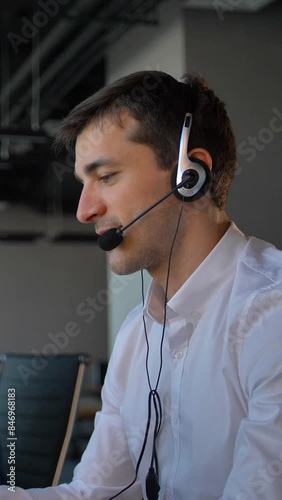 Attractive worker in office call center talking with client and then smile to camera. Concept of successful and cheerful solving of customer problems online. Vertical shot.