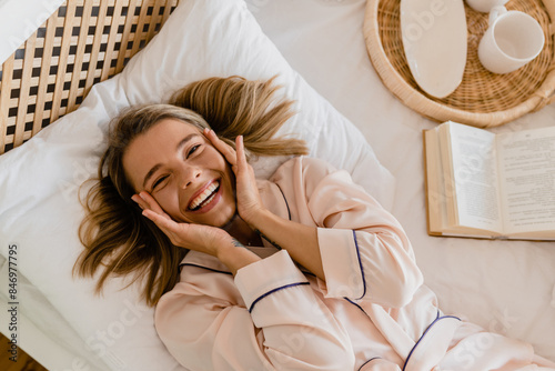 pretty smiling woman relaxing at home on bed in morning in pajamas