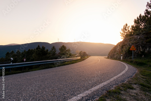 Mountain road at colorful sunset in summer. Beautiful curved roadway. Empty highway through the mountains with wind turbines in the background.