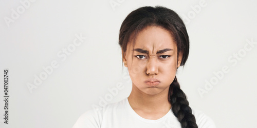 Фотография African American young girl with a braided ponytail is displaying an expression of anger on her face, with narrowed eyes and a furrowed brow